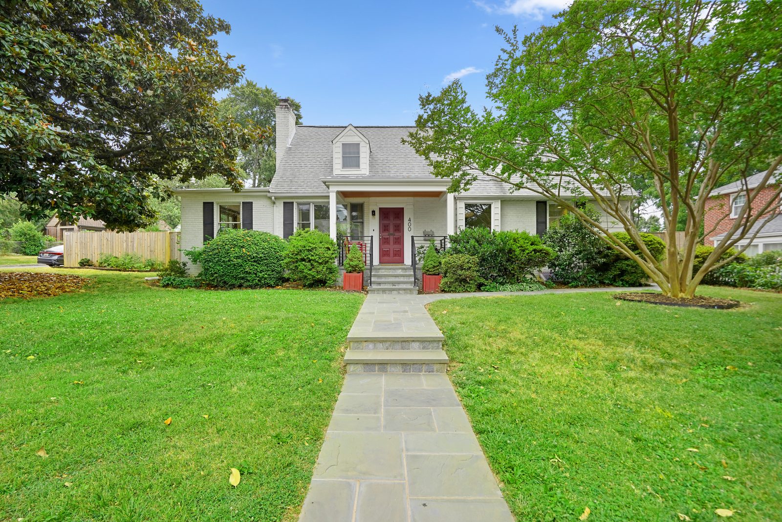 White brick cape with red door and flagstone path